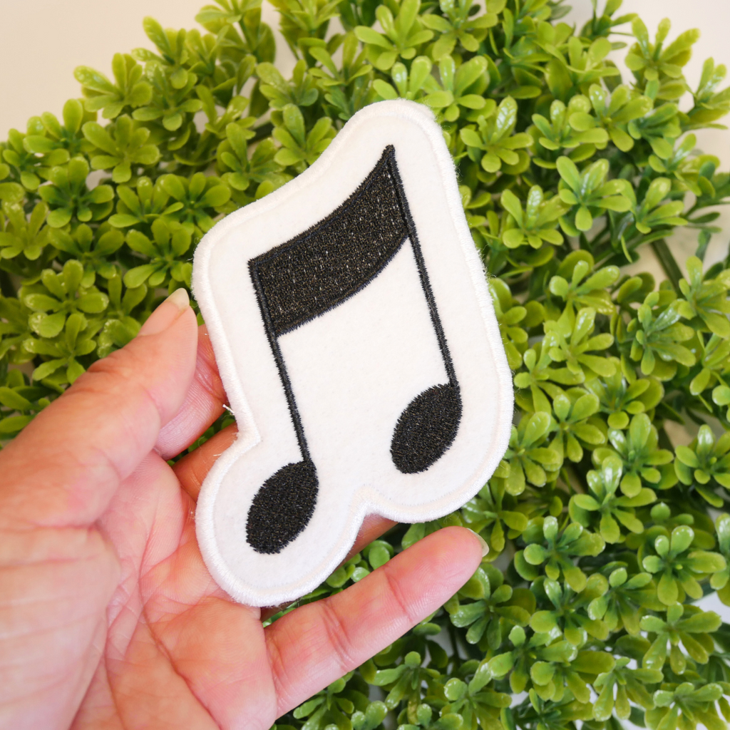 Music note patch held in a hand with green foliage in the background