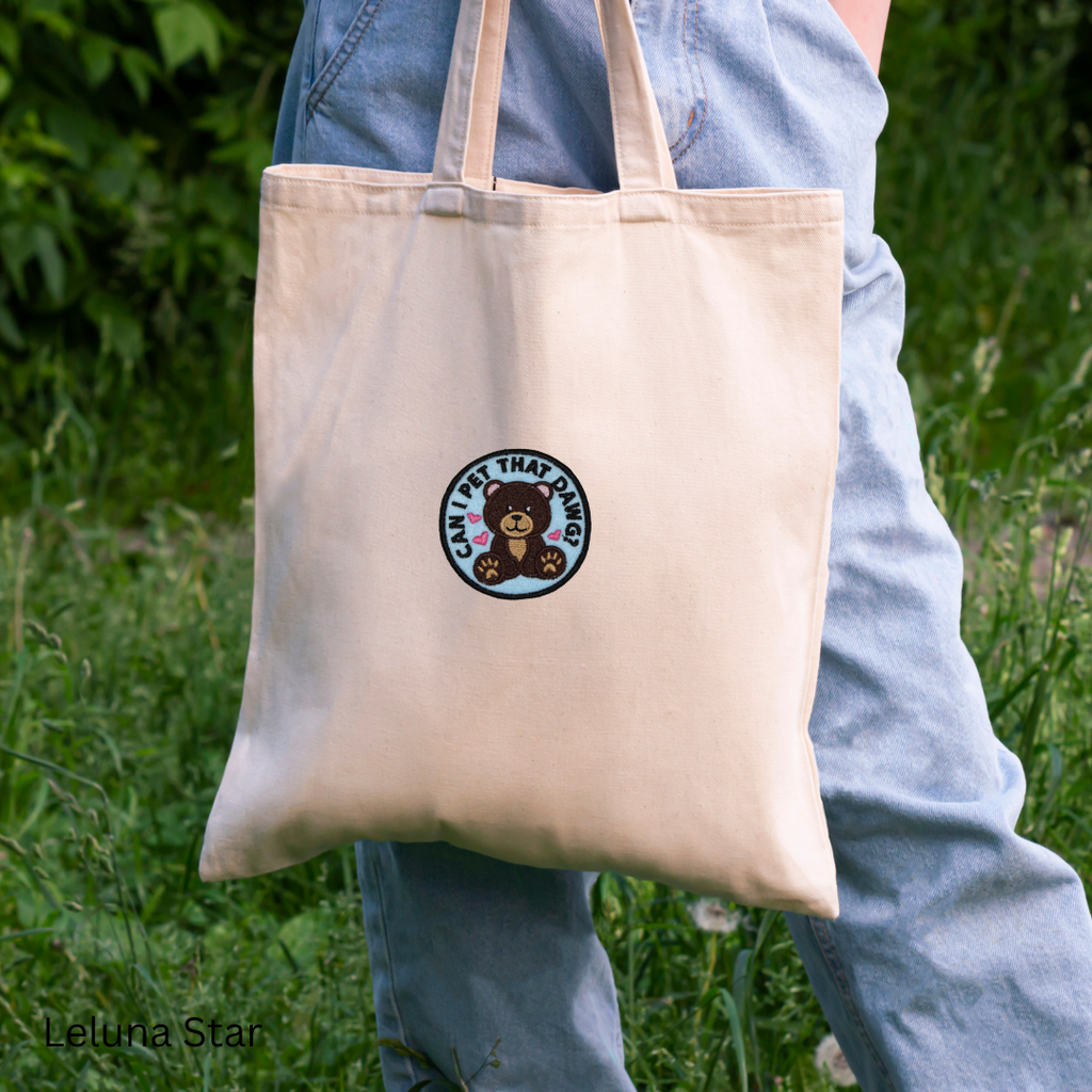 Beige tote bag with a logo held by a person in an outdoor setting