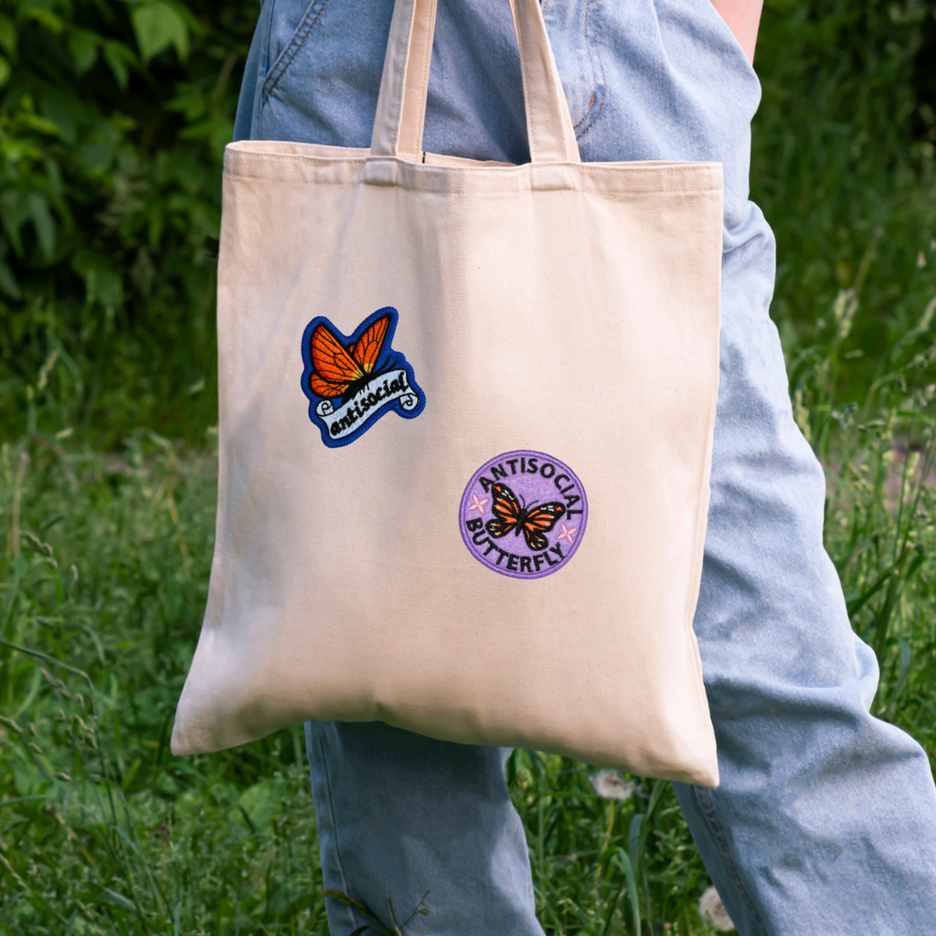 Tote bag with butterfly designs held by a person outdoors