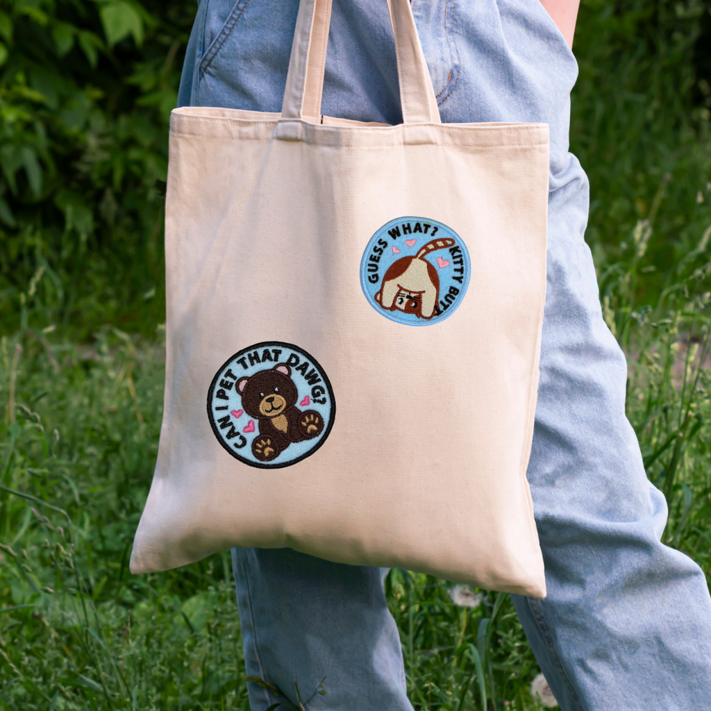 Beige tote bag with cartoon bear designs held by a person in a natural setting
