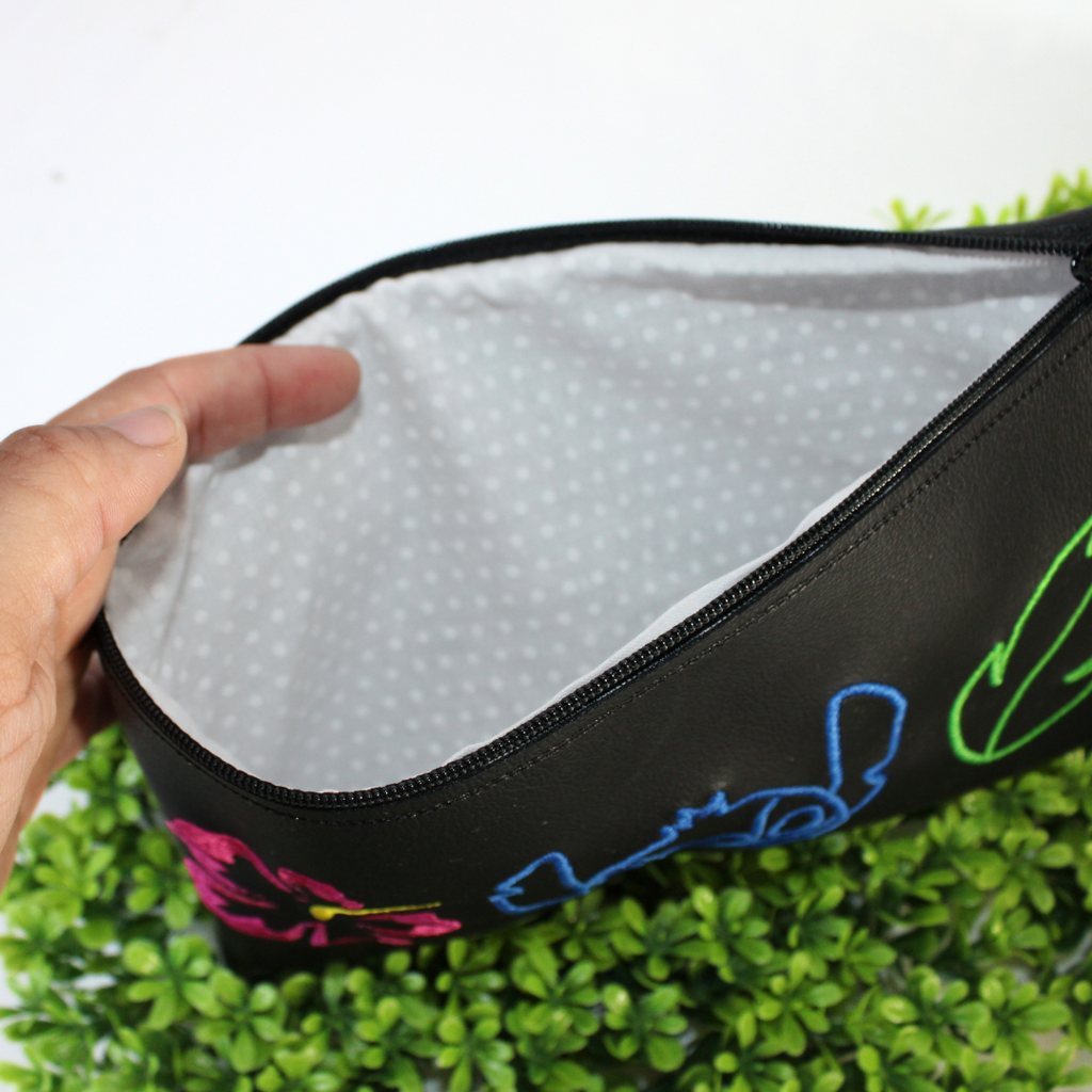 Black pouch with colorful designs of a character and plants on green foliage