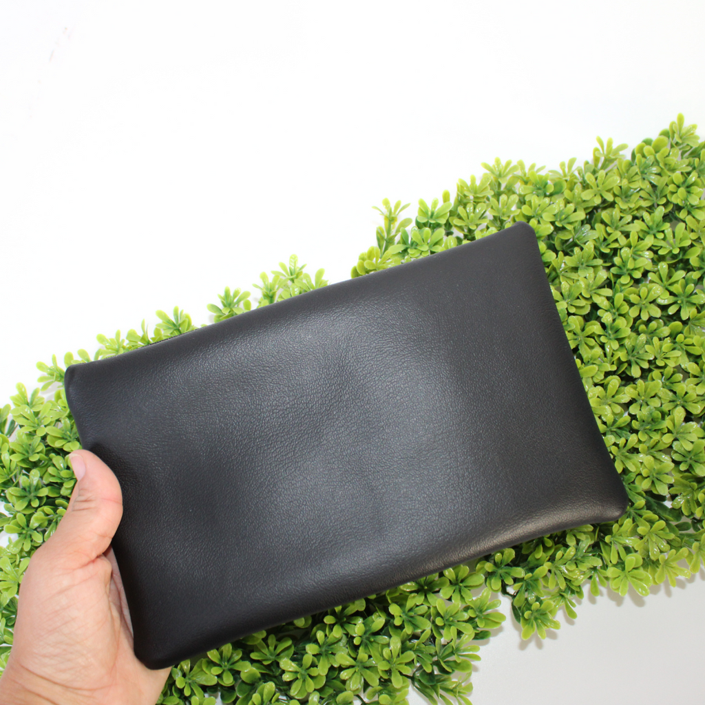 Black pouch with colorful designs of a character and plants on green foliage