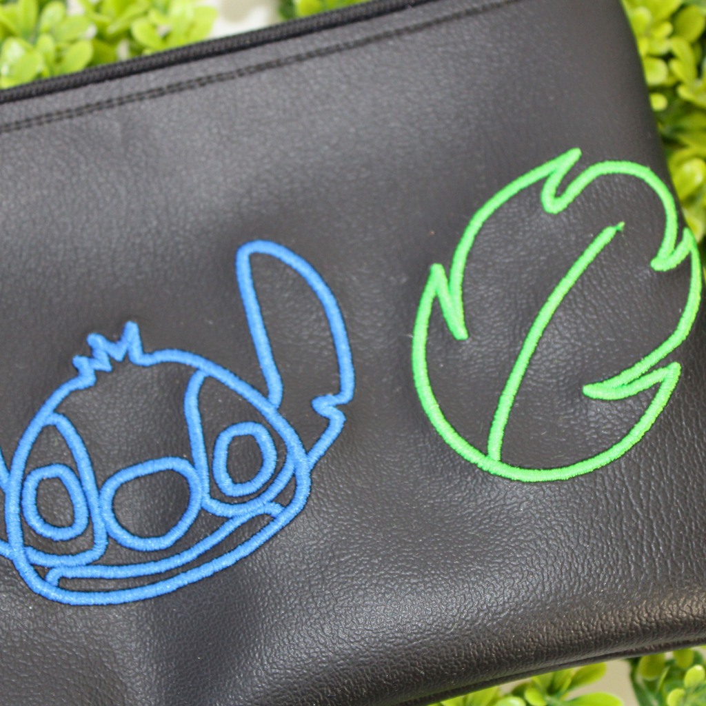 Black pouch with colorful designs of a character and plants on green foliage