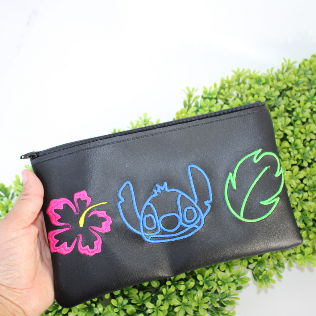 Black pouch with colorful designs of a character and plants on green foliage