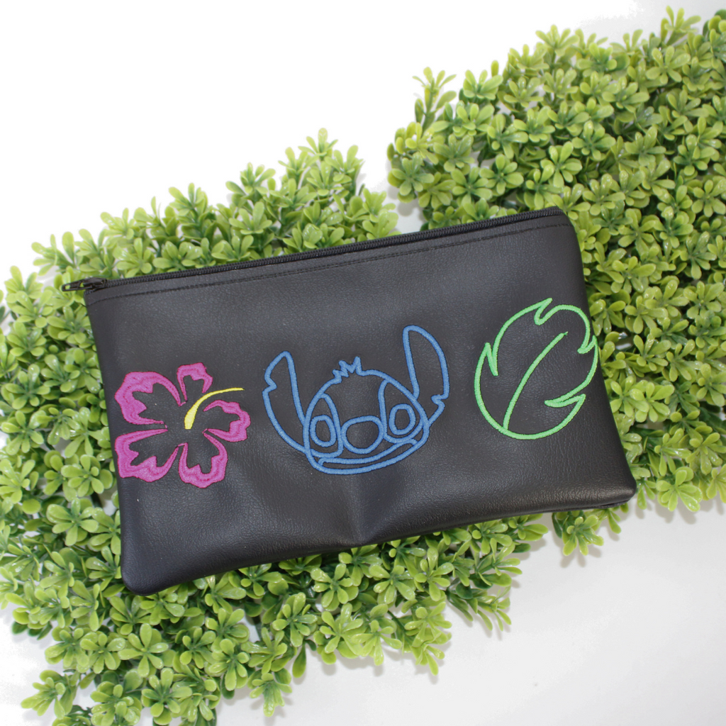 Black pouch with colorful designs of a character and plants on green foliage