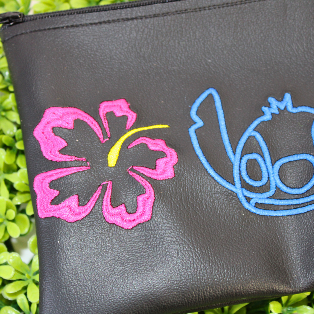 Black pouch with colorful designs of a character and plants on green foliage