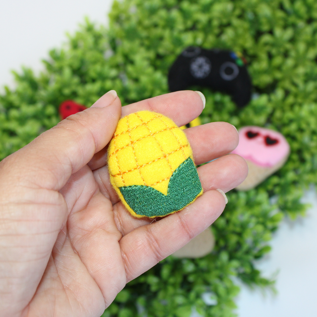 Hand holding a small yellow corn-shaped toy with a green base against a blurred green background.
