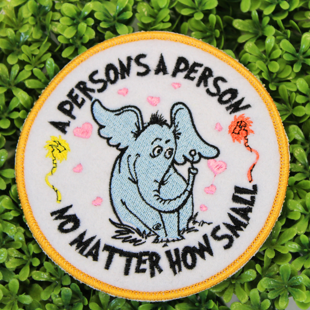 Circular patch with an elephant illustration and text on a green leaf background