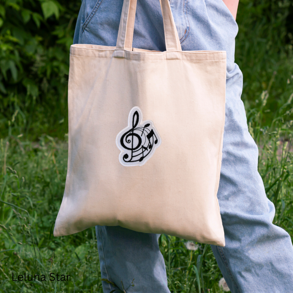 Beige tote bag with a music note design held by a person outdoors.