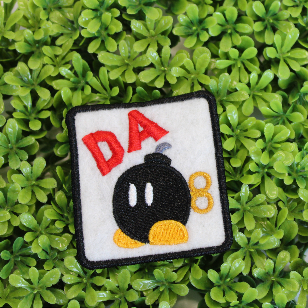 Embroidered patch with a bomb design and 'DA' text on a green leaf background