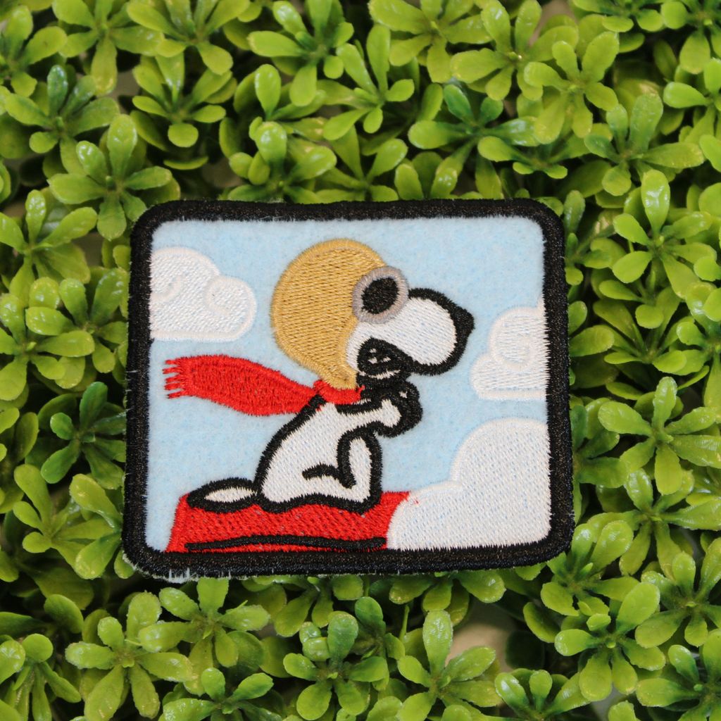 Embroidered patch of a dog with a red scarf on green leaves