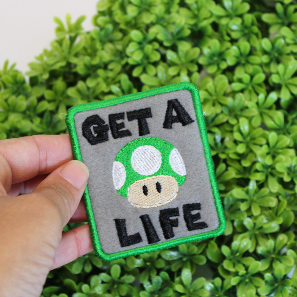 Patch with green mushroom and 'GET A LIFE' text held over green foliage