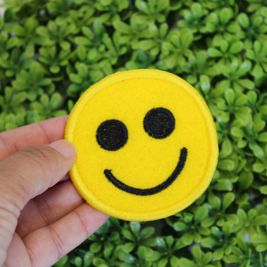 Smiley face patch held in front of green foliage