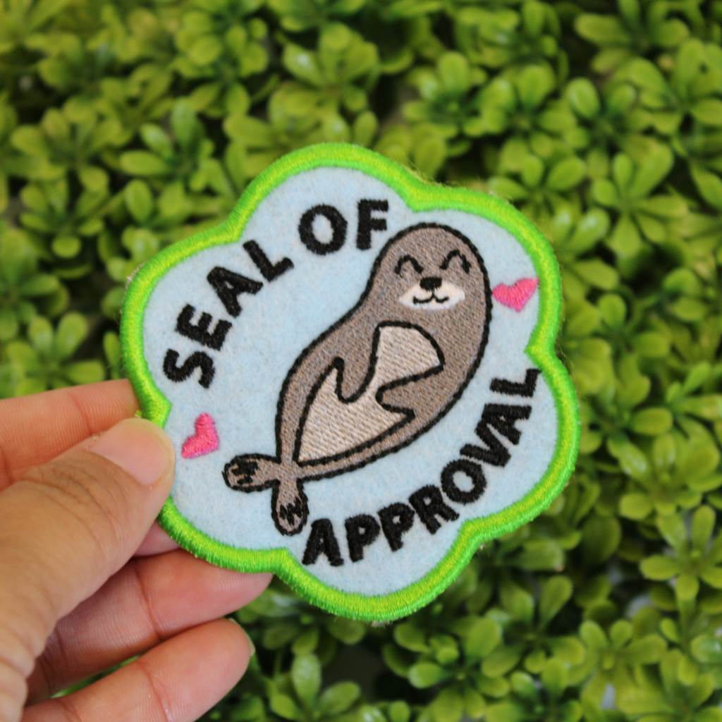 Patch with a seal design and 'Seal of Approval' text held in front of green foliage