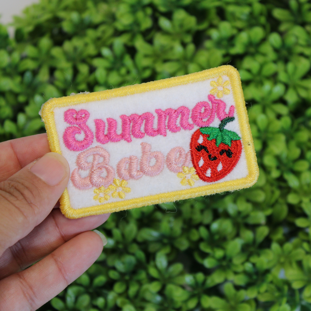 Embroidered patch with 'Summer Babe' and a strawberry held in front of green foliage