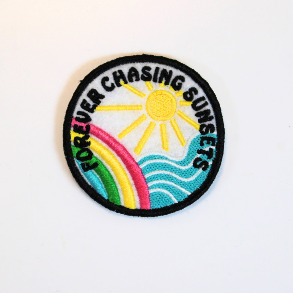 Embroidered patch with sun, rainbow, and text 'Forever Chasing Sunsets' on a white background