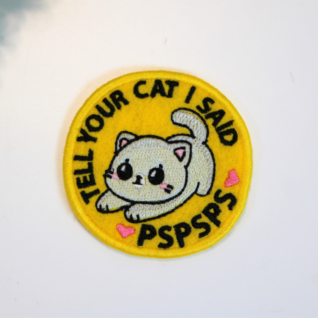 Embroidered patch with a cat illustration and text on a yellow background